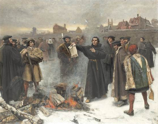 Luther holds a document over a bonfire in a snowy town square while a crowd watches