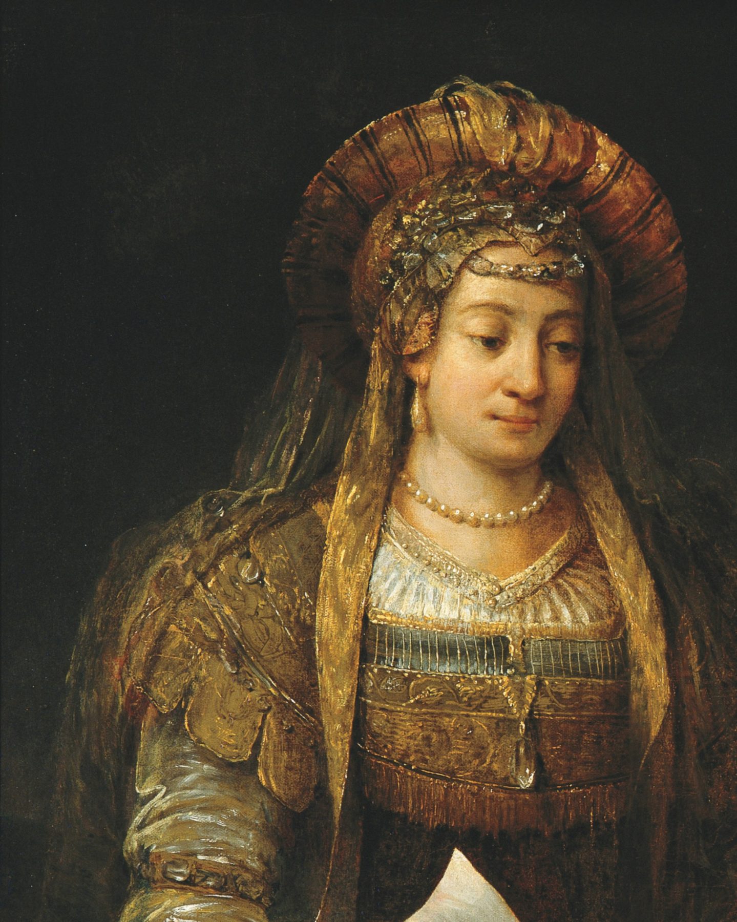 A painting by Aert de Gelder: Esther, a young woman with a calm face and lowered eyes, wears a tall striped turban of red and gold bound with a jewelled band, a golden veil falling to her shoulders, pearl earrings and a string of pearls, and a gown of olive and gold brocade. She holds a letter. The background is dark.