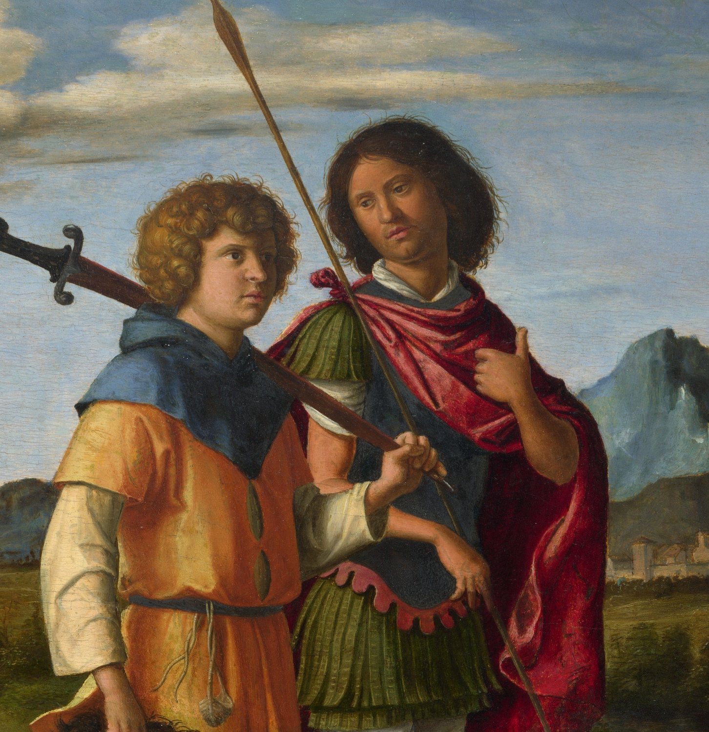 A painting by Cima da Conegliano: two young men walk side by side under a blue sky with white clouds. On the left, a curly-haired youth in an orange tunic and a blue cloak carries a great sword over his shoulder. On the right, Jonathan, dark-haired, in a red cloak over a green tunic, looks out calmly. A long spear rises between them. Blue mountains and a town lie behind.
