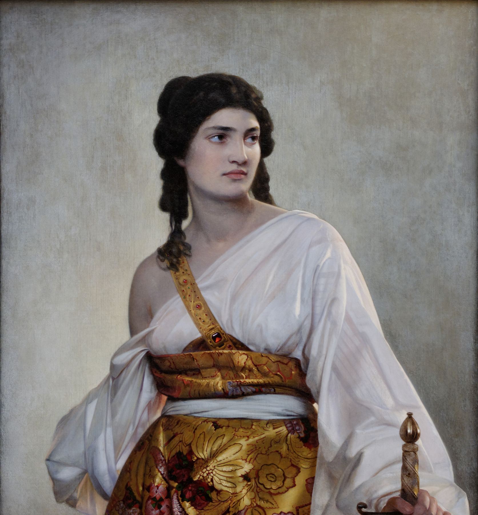 A painting by August Riedel: Judith, a young woman with dark hair in long braids, looks back over her shoulder with a steady gaze. She wears a loose white robe, a red and gold sash across one shoulder and a skirt of gold brocade. Her right hand rests on the hilt of a sword.