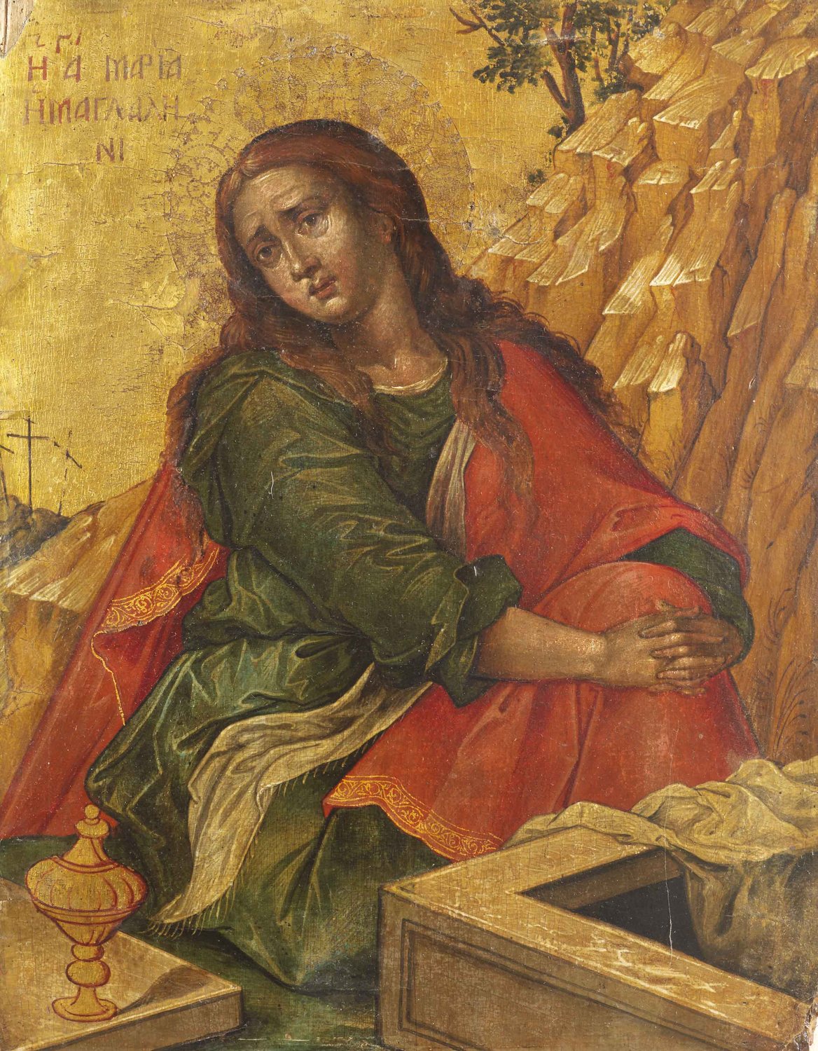 A Greek icon on a gold ground: Mary Magdalene, with long auburn hair, sits beside an empty stone tomb with her hands clasped over her knees, looking up in sorrow. She wears a green dress under a red cloak. A golden jar of ointment stands on the tomb's lid. Pale rocks and a small tree rise behind her, and three little crosses stand on a hill at the left.