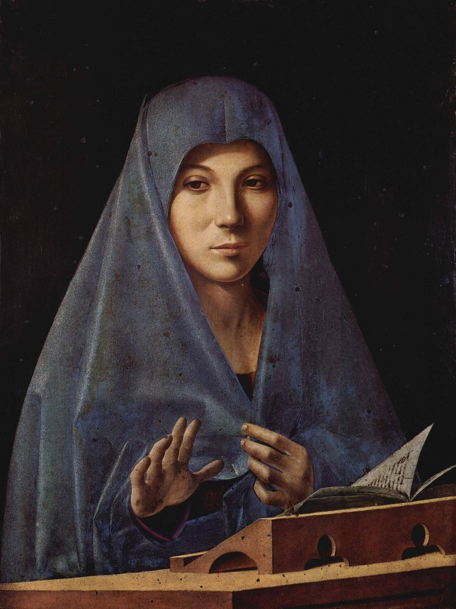 A painting by Antonello da Messina: Mary, a young woman in a blue veil drawn close around her face, looks out calmly to one side. One hand is raised, the other holds her blue mantle closed. A book lies open on a stand before her.
