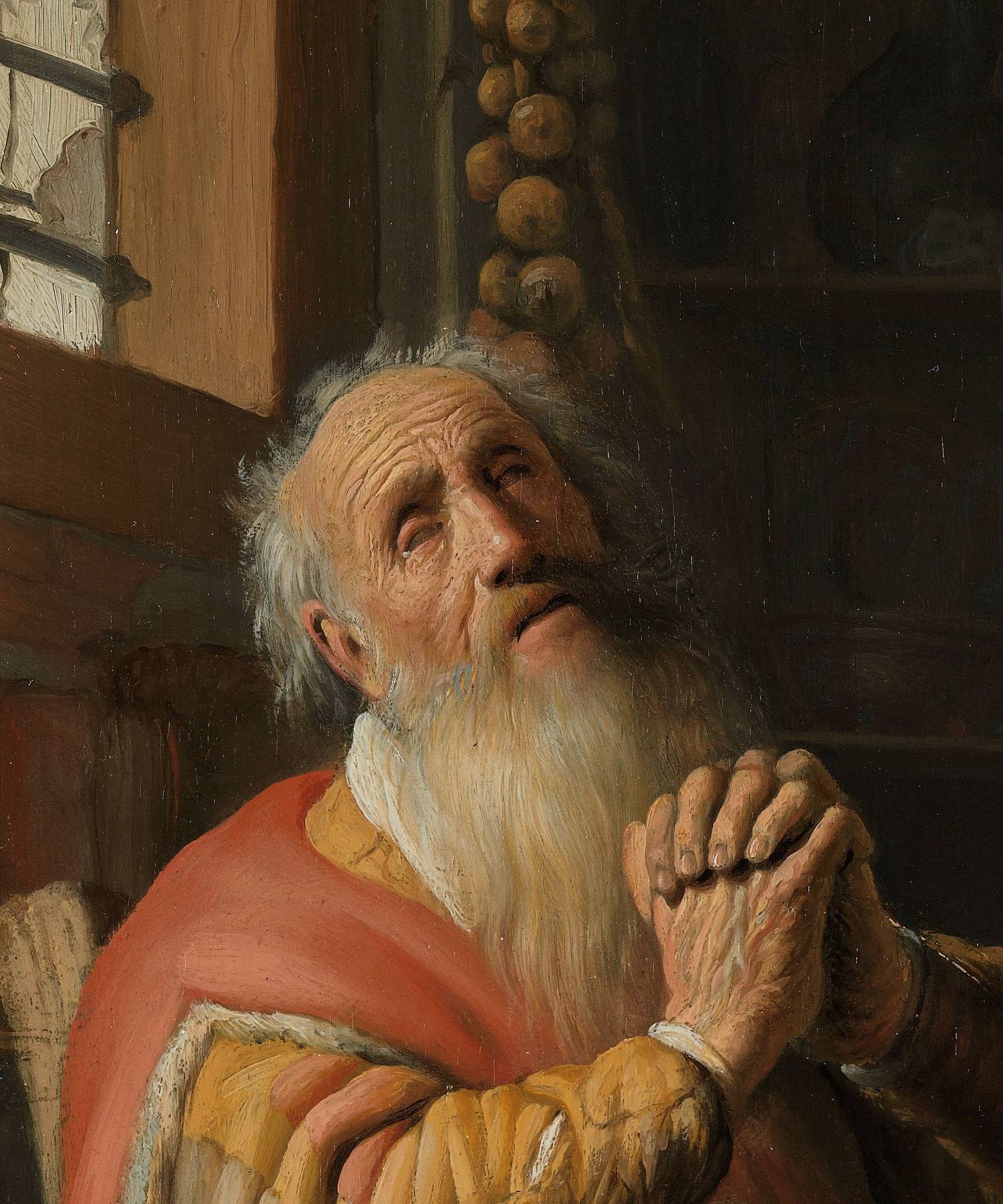 A detail of a painting by Rembrandt: Tobit, an old man with a long white beard and wisps of white hair, turns his blind eyes upward and clasps his hands in prayer. He wears a red cloak over a yellow coat. Behind him are a window and a dim room.