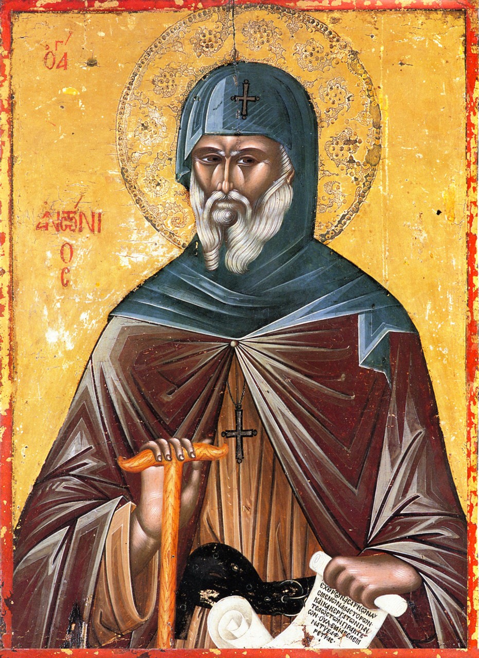 An icon on gold: Saint Antony with a long white beard, in a dark blue monk's hood marked with a cross and a brown cloak, holds a staff and an open scroll with Greek writing