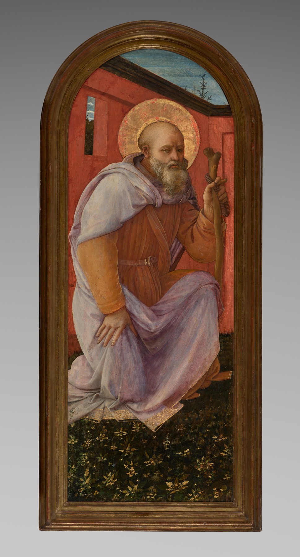 Saint Antony, a bald old man with a grey beard and a halo, in a violet cloak over an orange habit, kneels on a flowered lawn and holds a T-shaped staff hung with prayer beads, by Fra Filippo Lippi