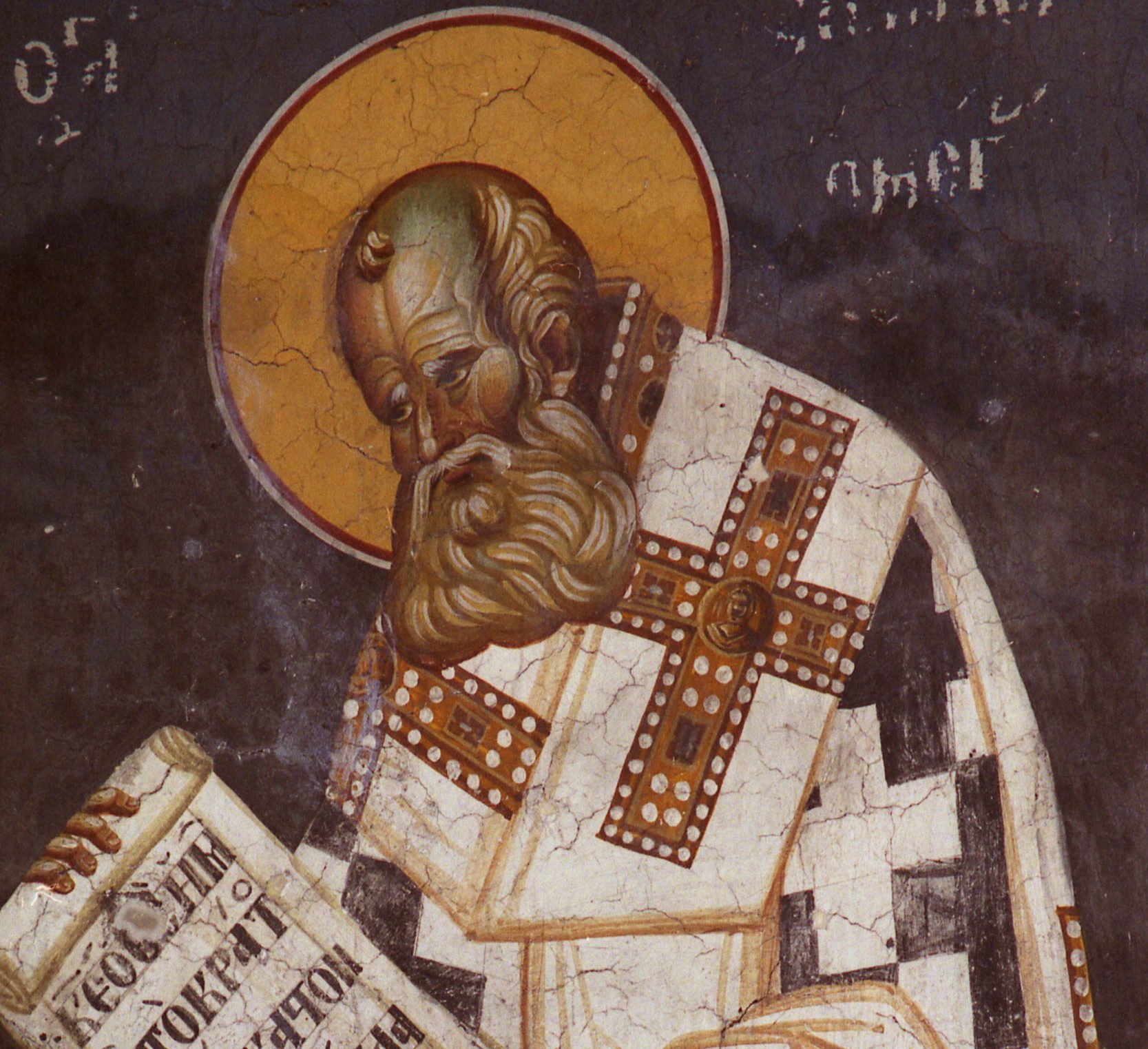 A Byzantine fresco: Athanasius, bald, with a curling beard, bows his head low before a gold halo on a deep blue wall. He wears a white vestment with large red crosses and holds an open scroll written in Greek. His name is painted beside his halo.