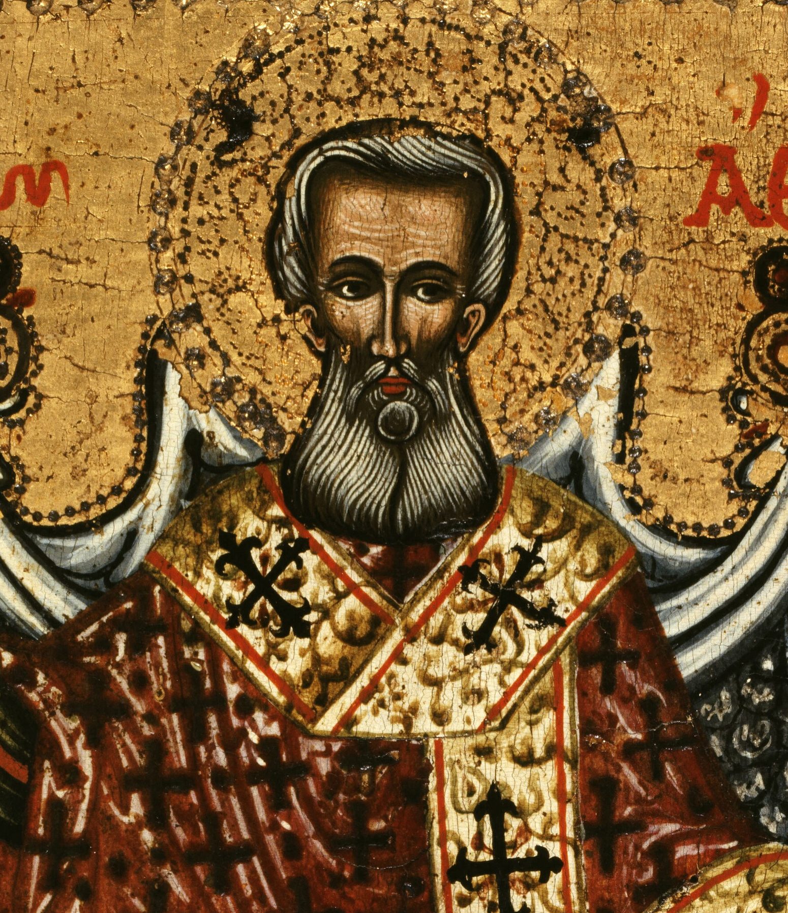 A Greek icon: Saint Athanasius, a bishop with a long grey and black beard, dark brows and steady eyes, before a gold halo. He wears a red and gold vestment with black crosses on his shoulders. His name is written in red Greek letters beside his head.