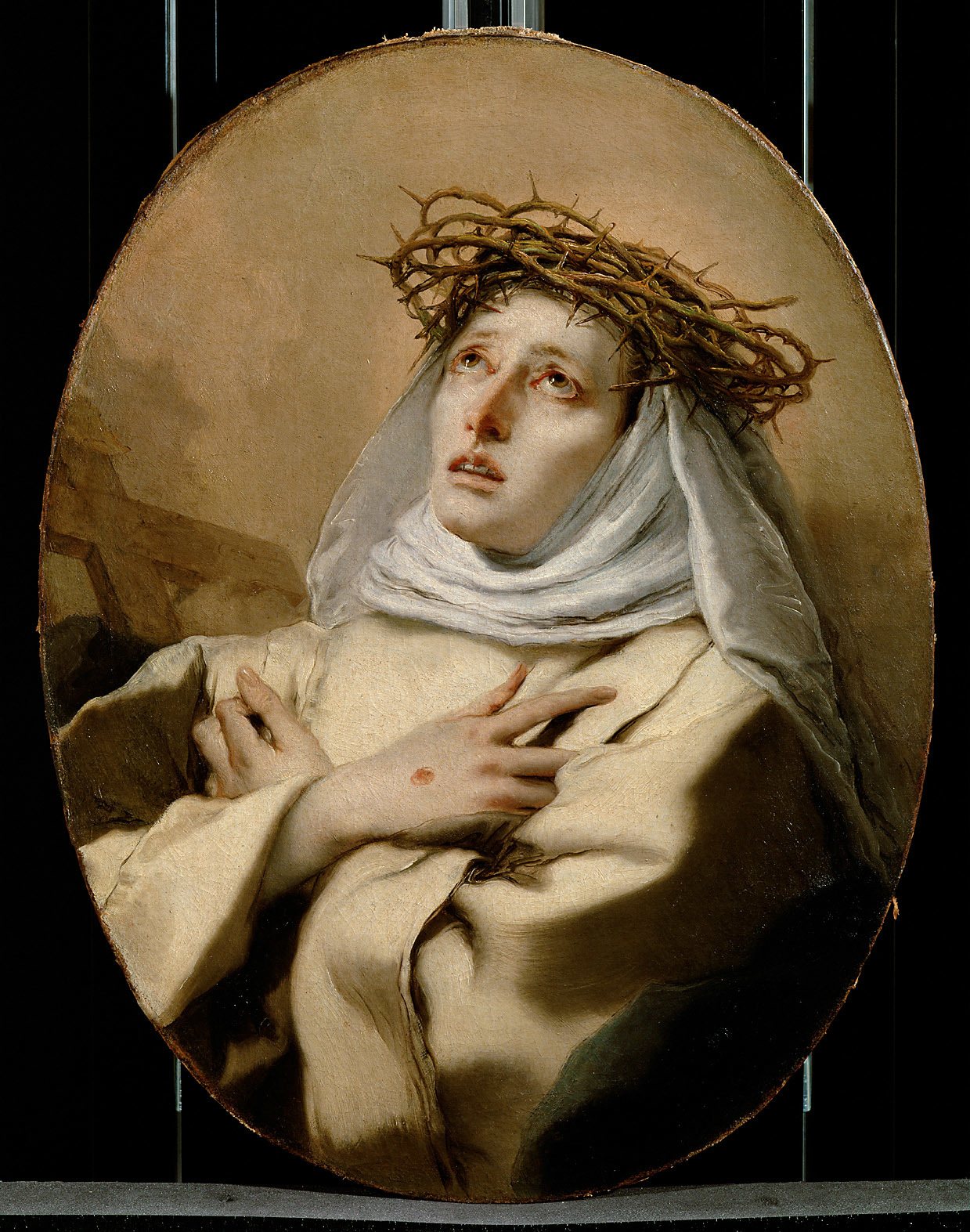 An oval oil painting: Catherine looks up with parted lips and reddened eyes, a crown of thorns on her white veil, her hands crossed on her breast, a small red wound on the back of one hand