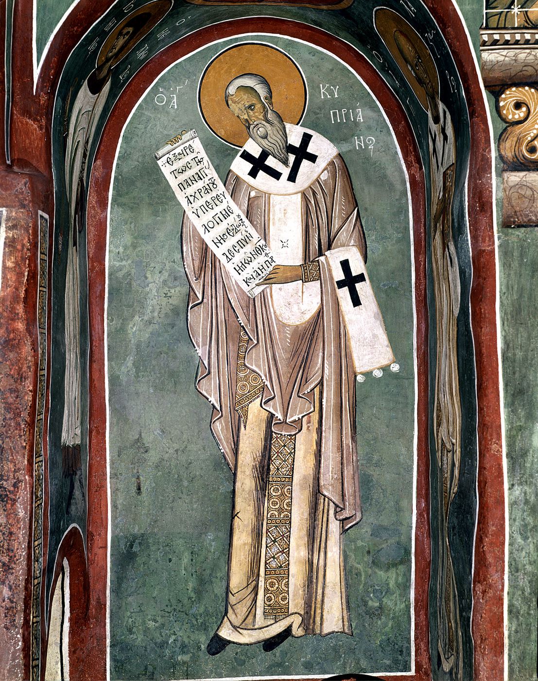 A Byzantine fresco of a grey-bearded bishop with a gold halo, in pale robes and a white stole marked with black crosses, holding an open scroll; Greek letters beside him read Saint Cyprian