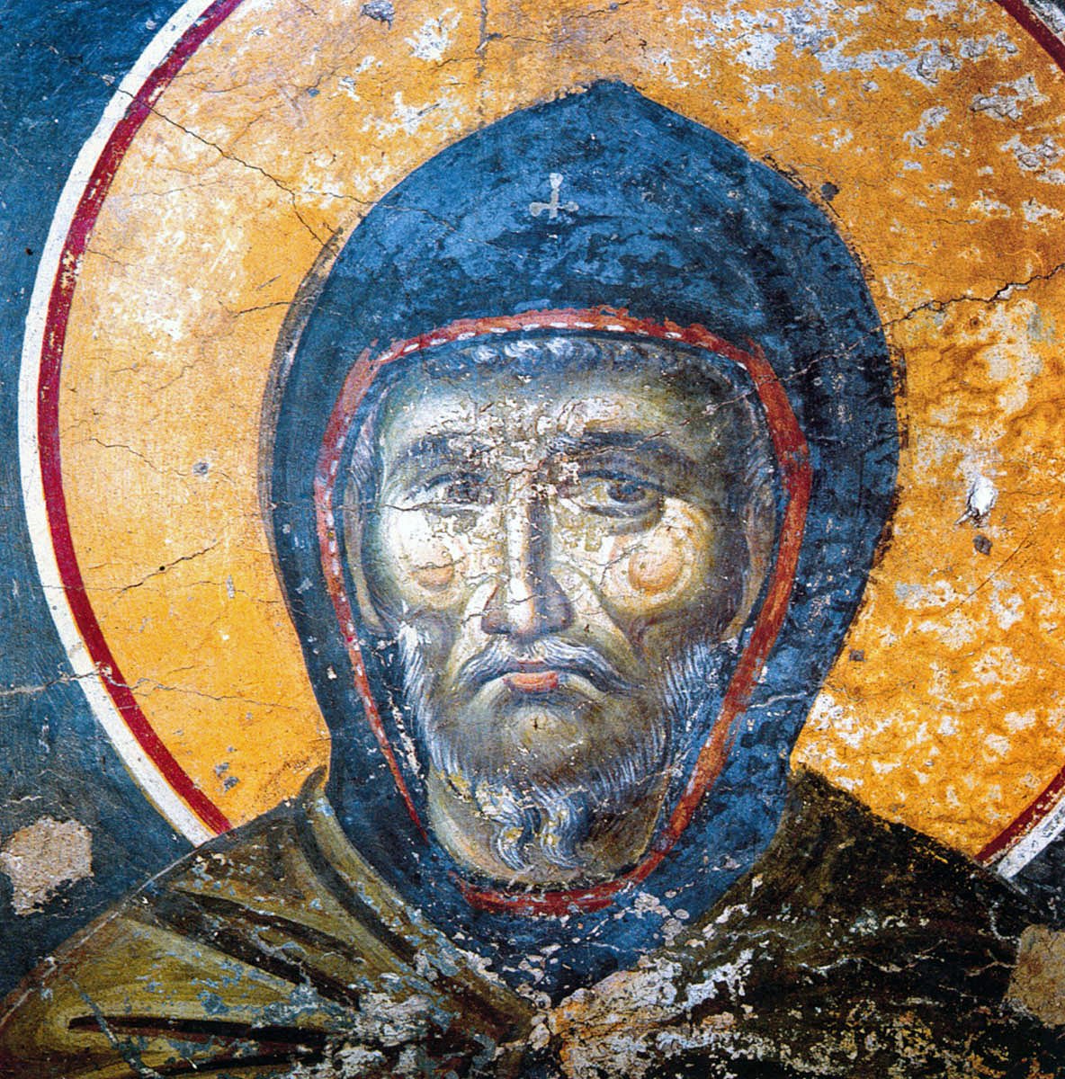 Fresco of St Ephrem the Syrian in a blue monk's hood edged in red, his lined face grave, against a gold halo with cracked plaster