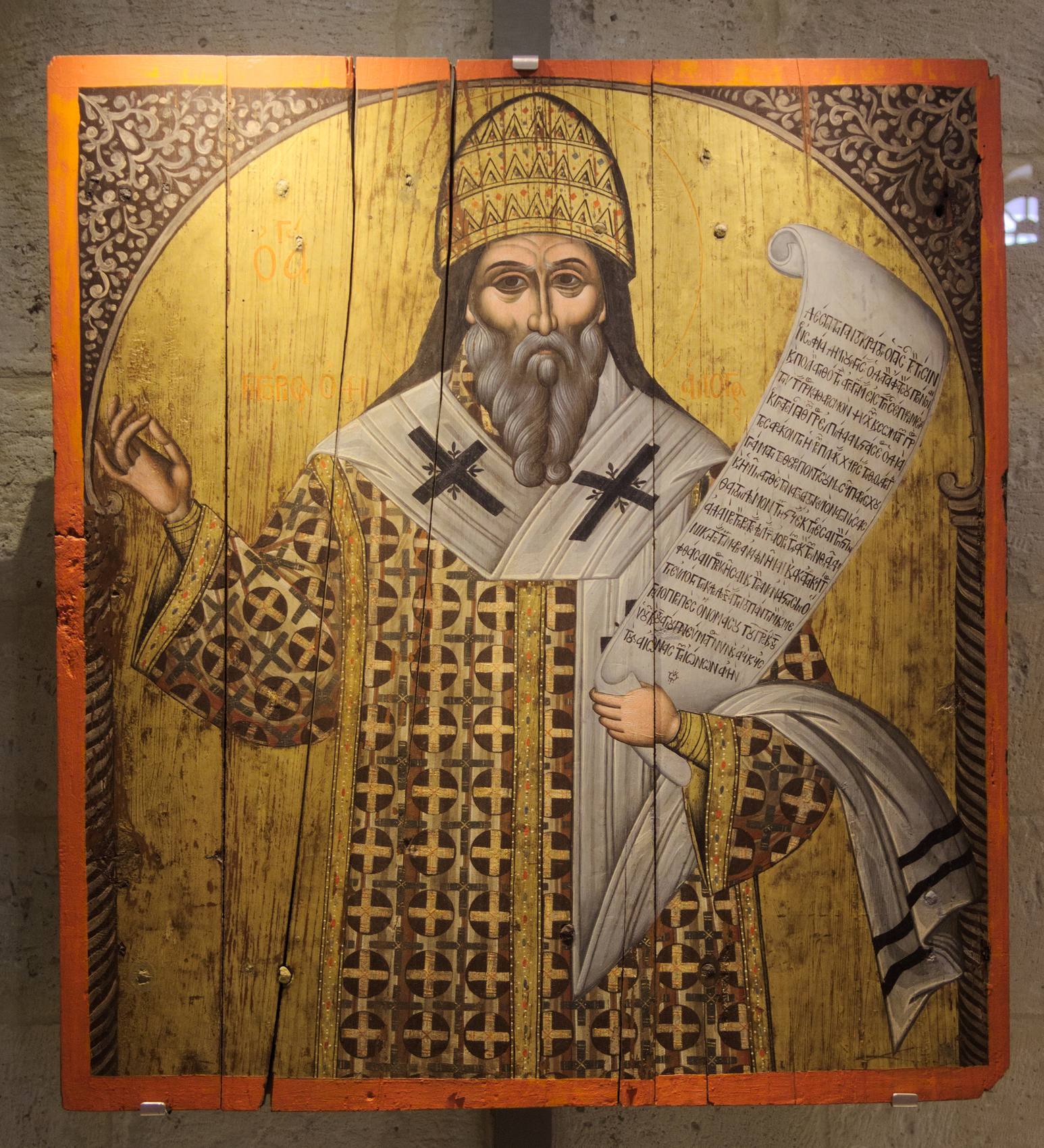 A Greek icon of Gregory the Dialogist: a grey-bearded bishop in a gold crown and a white stole with black crosses raises his right hand and holds a long scroll of Greek writing, on a gold ground
