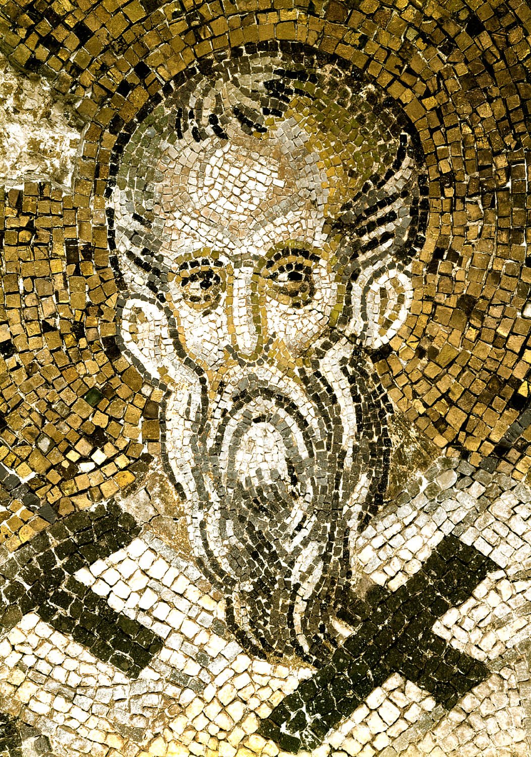 A Byzantine mosaic of glittering gold and silver-white stones: the head of Saint Ignatius, an old bishop with a high bald forehead, wide dark eyes and a long pointed beard, above a white stole marked with black crosses