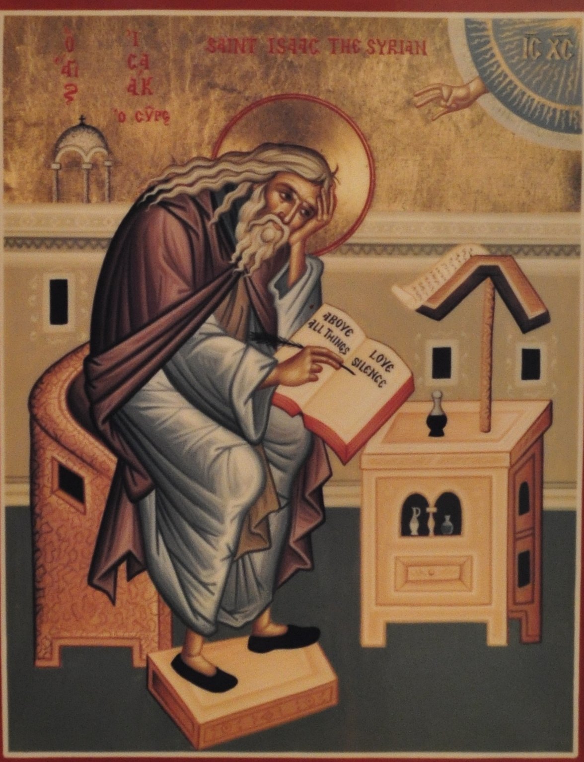 An icon of Saint Isaac the Syrian: an old monk with long white hair and beard sits at a lectern, his head resting on his hand, writing in an open book lettered with a line about silence, while a hand of blessing reaches down from heaven in the corner