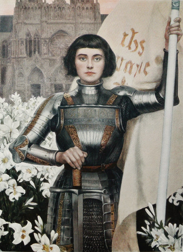 A coloured print: Joan, with short dark hair, stands in shining armour among white lilies, one hand on the hilt of her sword and the other holding the pole of a white banner, with a Gothic cathedral behind her; the names of Jesus and Mary are on her breastplate and banner