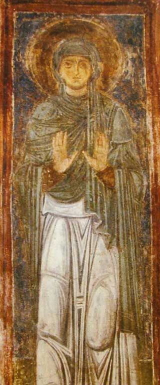A fresco of Macrina standing in a grey-green veil and cloak over a white robe, a gold halo behind her head, both hands raised with the palms facing out.