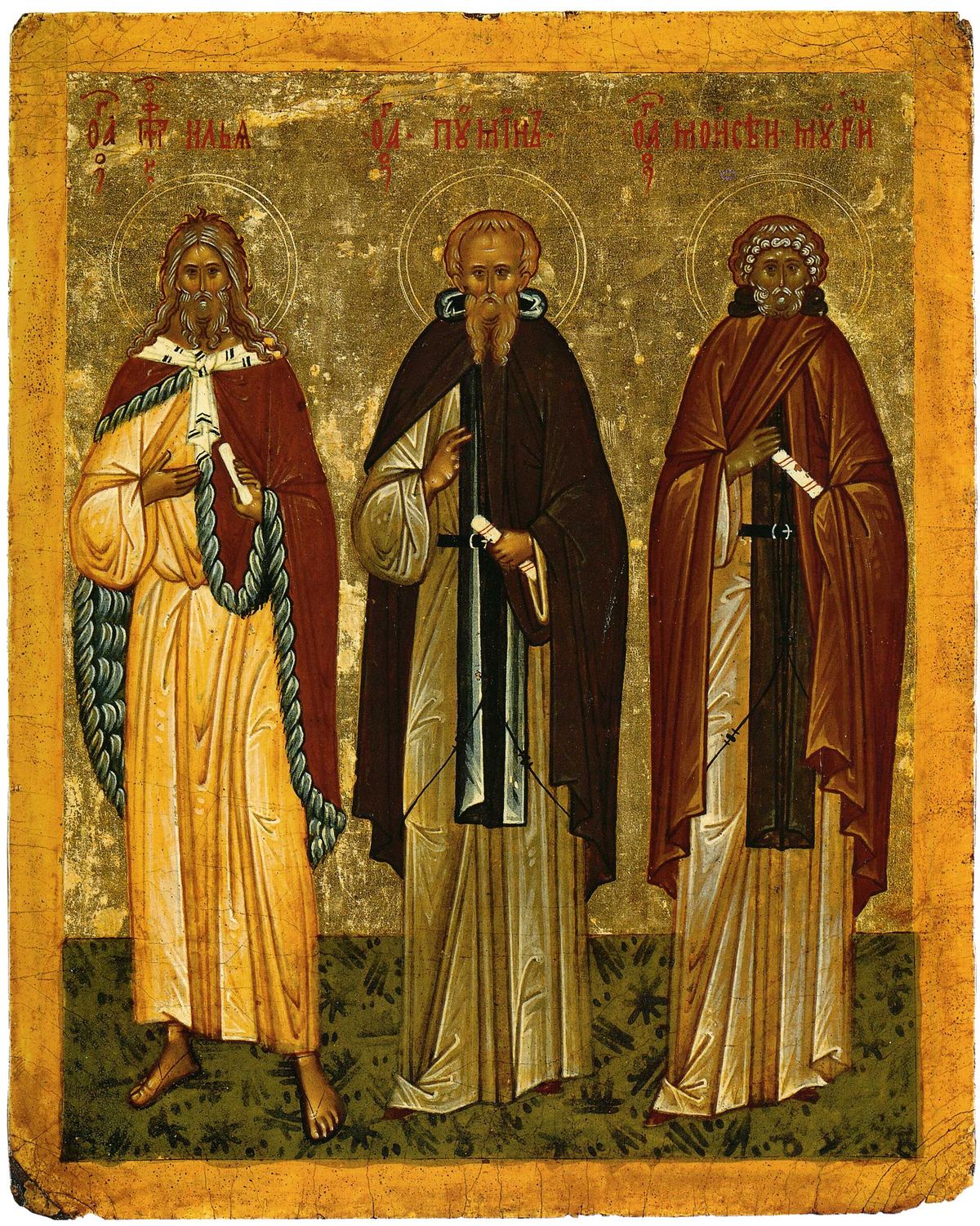 An icon on a gold ground: three standing saints. On the left the prophet Elijah in a yellow robe and red cloak, with long hair; in the middle Poemen in a dark monk's habit; on the right Moses, with white curly hair and a short white beard, in a red cloak, holding a scroll. Their names are lettered above them.