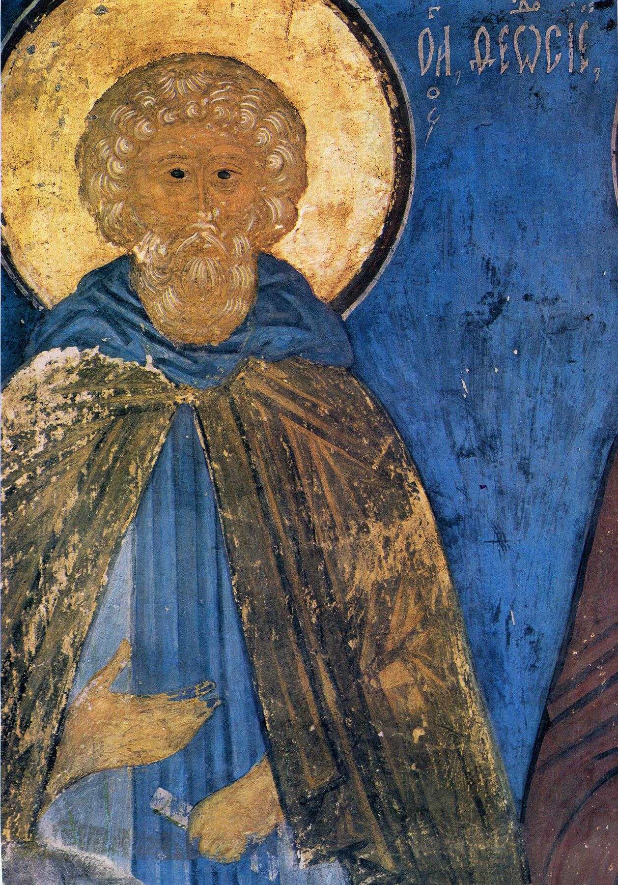 A fresco: Moses, an old monk with a round head of tight grey-white curls and a short curly beard, before a gold halo on a deep blue wall. He wears a blue robe under a dark, worn cloak and holds a small scroll. Old Slavonic letters beside his head name him.
